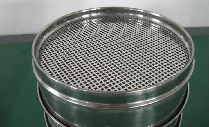 Stainless steel test sieve with a perforated plate on a green surface for comparing sieve specifications and quotes.